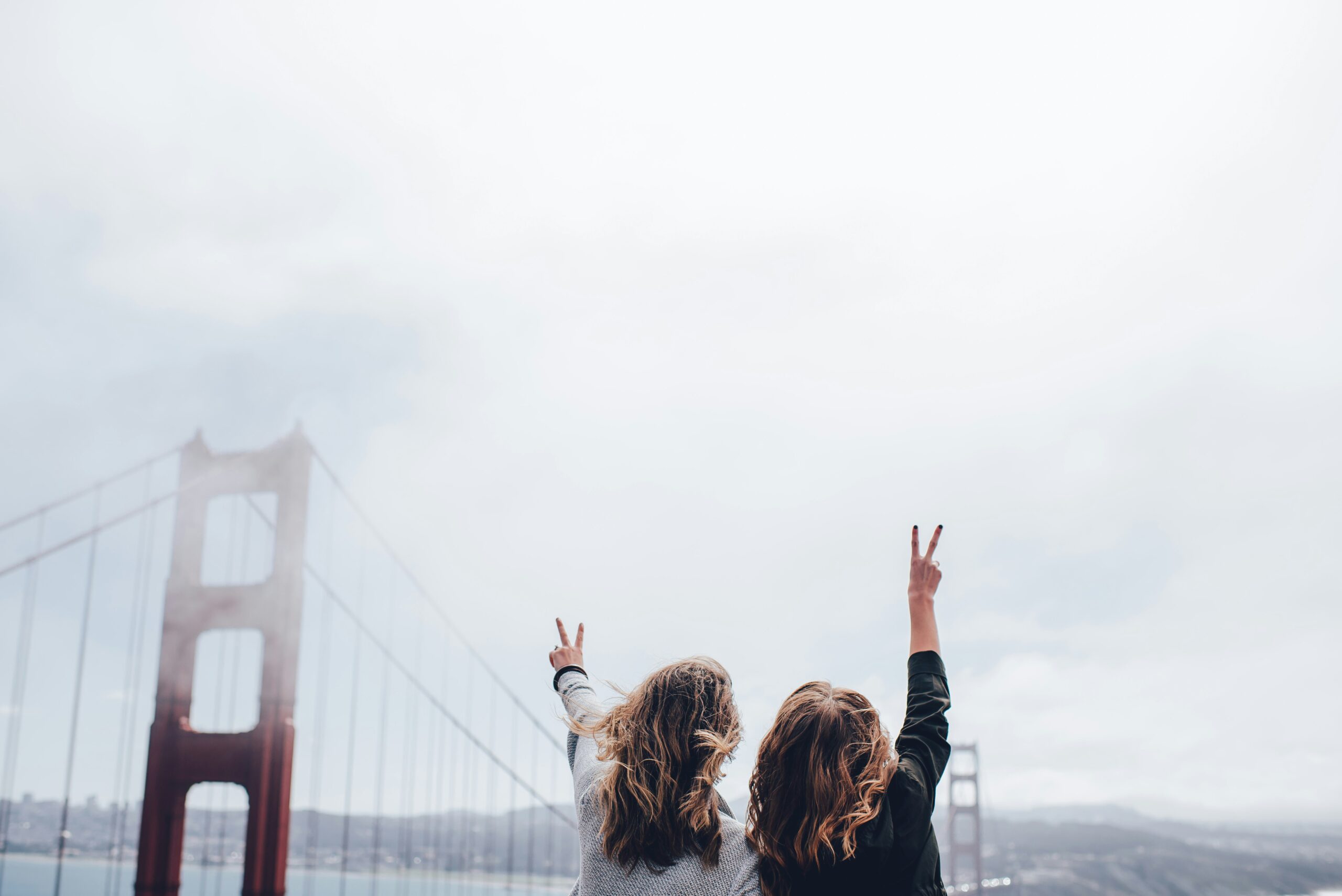 Two girls holding up peace signs with their hands near the Golden Gate Bridge